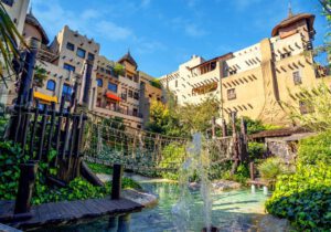 Afrika-inspiriertes Hotel mit Hängebrücke und Wasserfall im sonnigen grünen Garten, perfekter Urlaubsort für Familien.