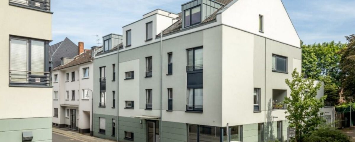 Moderne Wohngebäude an einer ruhigen Stadtstraße mit blauen Fensterelementen und grünen Akzenten.