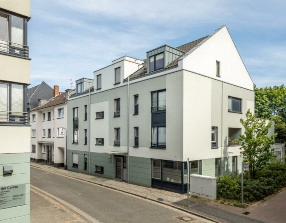 Moderne Wohngebäude an einer ruhigen Stadtstraße mit blauen Fensterelementen und grünen Akzenten.