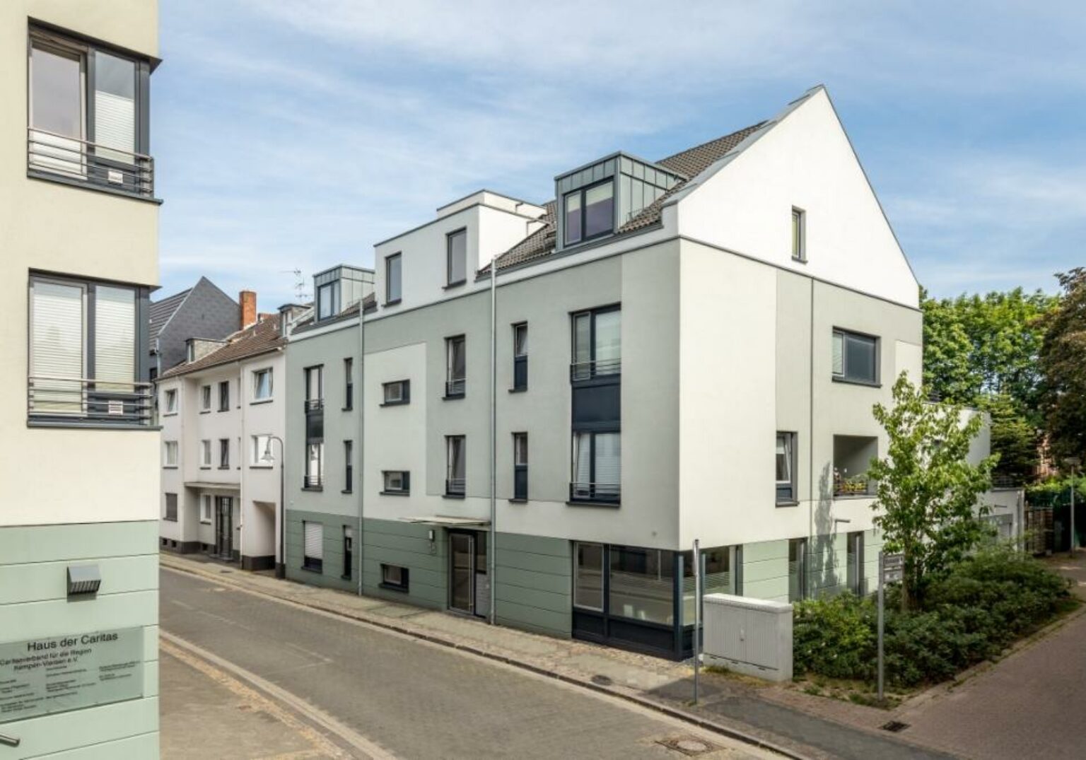 Moderne Wohngebäude an einer ruhigen Stadtstraße mit blauen Fensterelementen und grünen Akzenten.