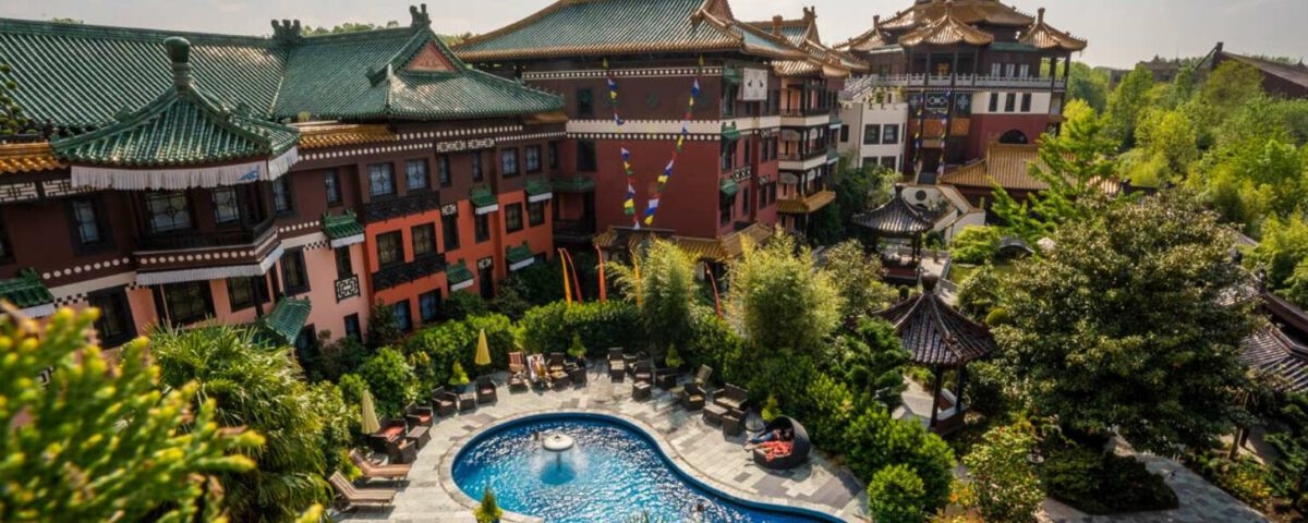 Asiatisch inspiriertes Hotel mit Pool und üppigen Gärten, umgeben von traditionellen Gebäuden an einem sonnigen Tag.