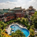 Asiatisch inspiriertes Hotel mit Pool und üppigen Gärten, umgeben von traditionellen Gebäuden an einem sonnigen Tag.