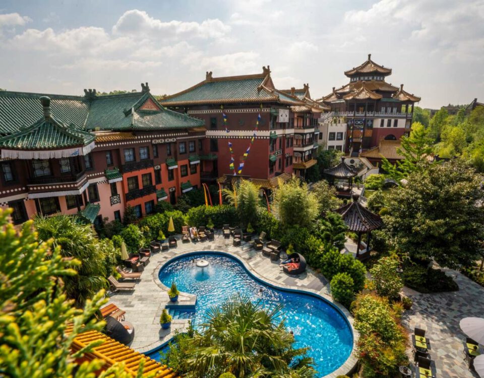 Asiatisch inspiriertes Hotel mit Pool und üppigen Gärten, umgeben von traditionellen Gebäuden an einem sonnigen Tag.