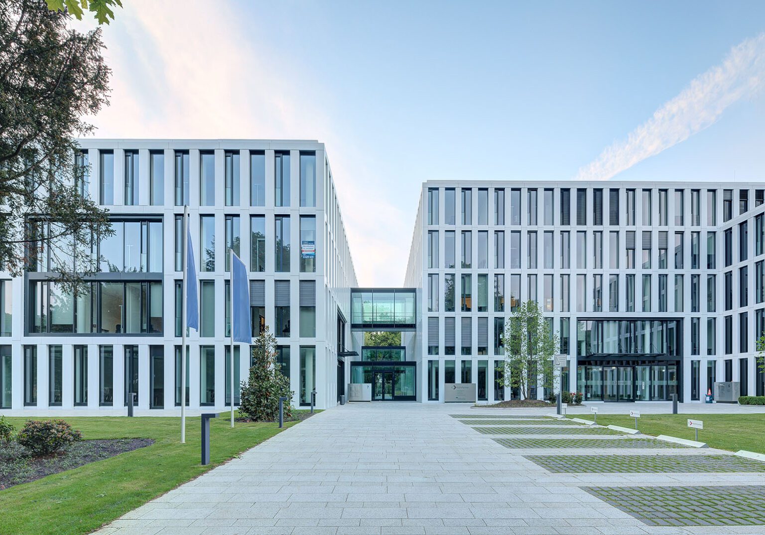 Moderne Bürogebäude mit Glasfronten, umgeben von Grünflächen und Gehweg im Vordergrund.