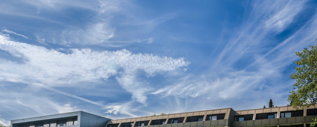 Modernes Hotelgebäude unter blauem Himmel, umgeben von grünen Wiesen, ideal für eine ruhige Auszeit.