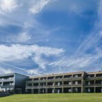 Modernes Hotelgebäude unter blauem Himmel, umgeben von grünen Wiesen, ideal für eine ruhige Auszeit.