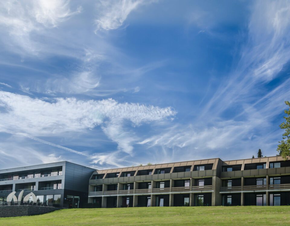Modernes Hotelgebäude unter blauem Himmel, umgeben von grünen Wiesen, ideal für eine ruhige Auszeit.