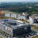 Luftaufnahme eines modernen Bürokomplexes mit im Bau befindlichen Gebäuden, umgeben von Natur und Grünflächen.