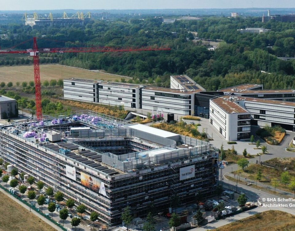 Luftaufnahme eines modernen Bürokomplexes mit im Bau befindlichen Gebäuden, umgeben von Natur und Grünflächen.