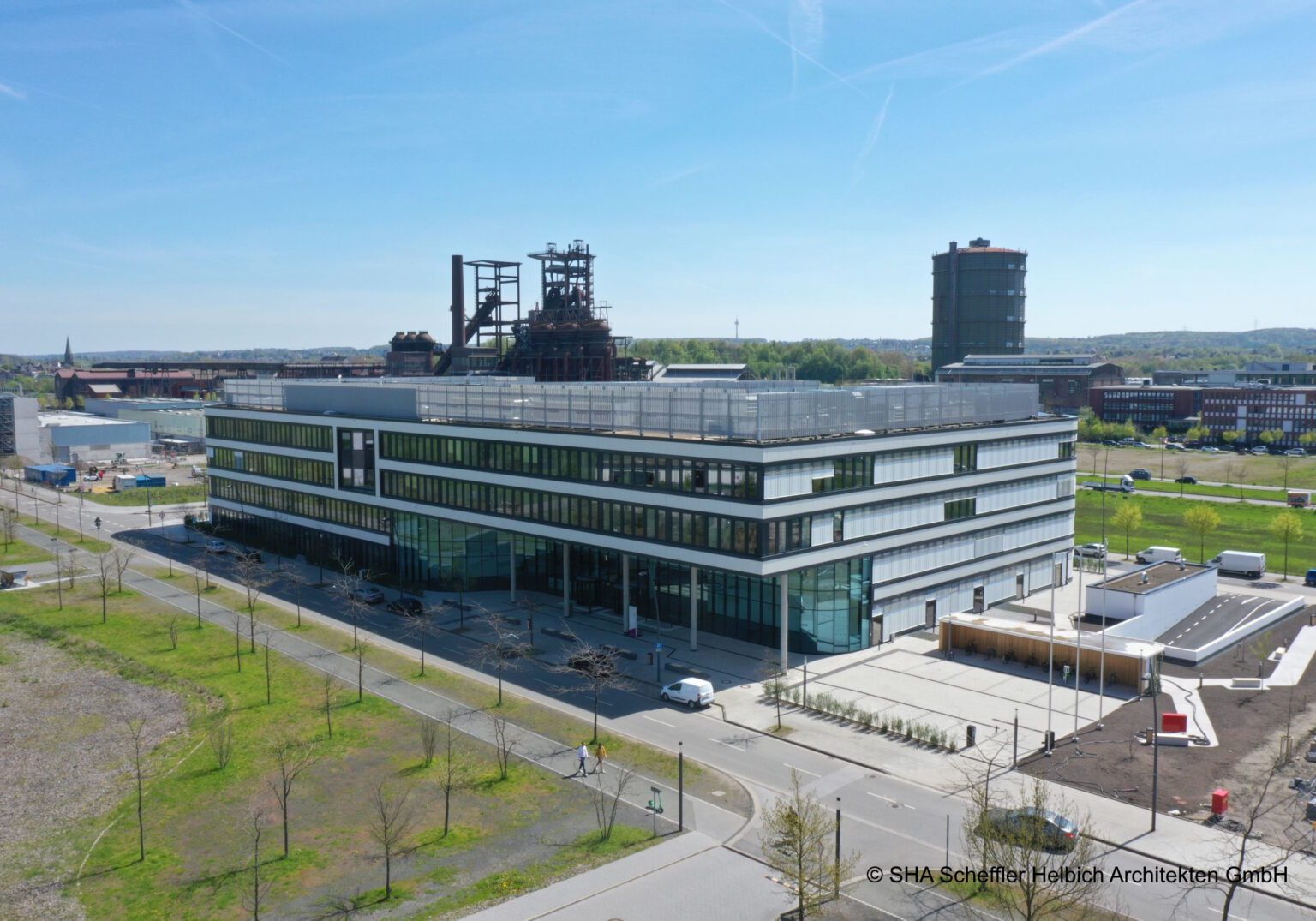 Modernes Bürogebäude in urbaner Umgebung mit industriellem Hintergrund und klarem Himmel.