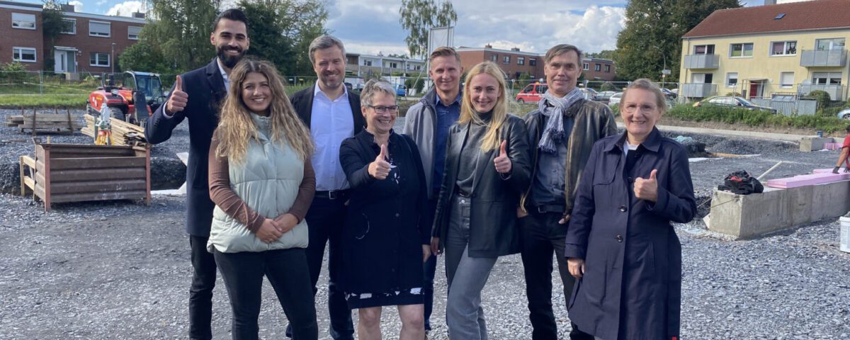 Gruppe von Menschen auf einer Baustelle an einem sonnigen Tag, alle zeigen einen Daumen hoch.