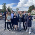 Gruppe von Menschen auf einer Baustelle an einem sonnigen Tag, alle zeigen einen Daumen hoch.