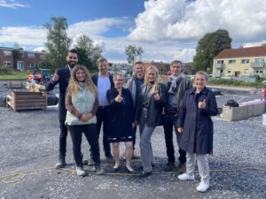 Gruppe von Menschen auf einer Baustelle an einem sonnigen Tag, alle zeigen einen Daumen hoch.