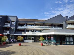 Modernes Gebäude mit Balkonen, blauem Himmel und Sitzgelegenheiten im Freien an einem sonnigen Tag.