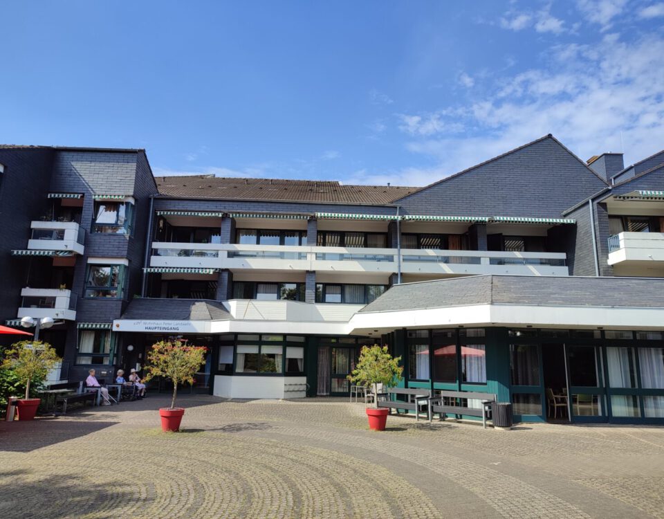 Modernes Gebäude mit Balkonen, blauem Himmel und Sitzgelegenheiten im Freien an einem sonnigen Tag.