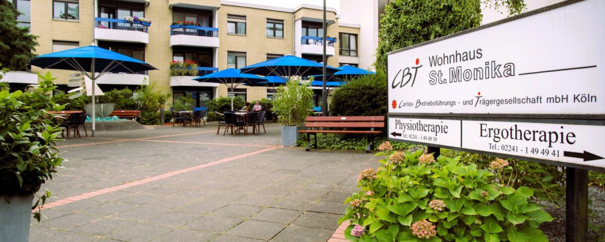 CBT Wohnhaus St. Monika mit blauen Sonnenschirmen, Hinweisschild zu Physiotherapie und Ergotherapie in Köln.