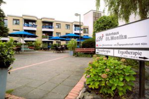 CBT Wohnhaus St. Monika mit blauen Sonnenschirmen, Hinweisschild zu Physiotherapie und Ergotherapie in Köln.