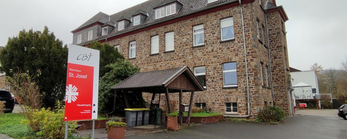 Mittelalterliches Steingebäude in Meckenheim mit Schild Wohnhaus St. Josef und Garten im Vordergrund.
