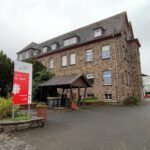 Mittelalterliches Steingebäude in Meckenheim mit Schild Wohnhaus St. Josef und Garten im Vordergrund.