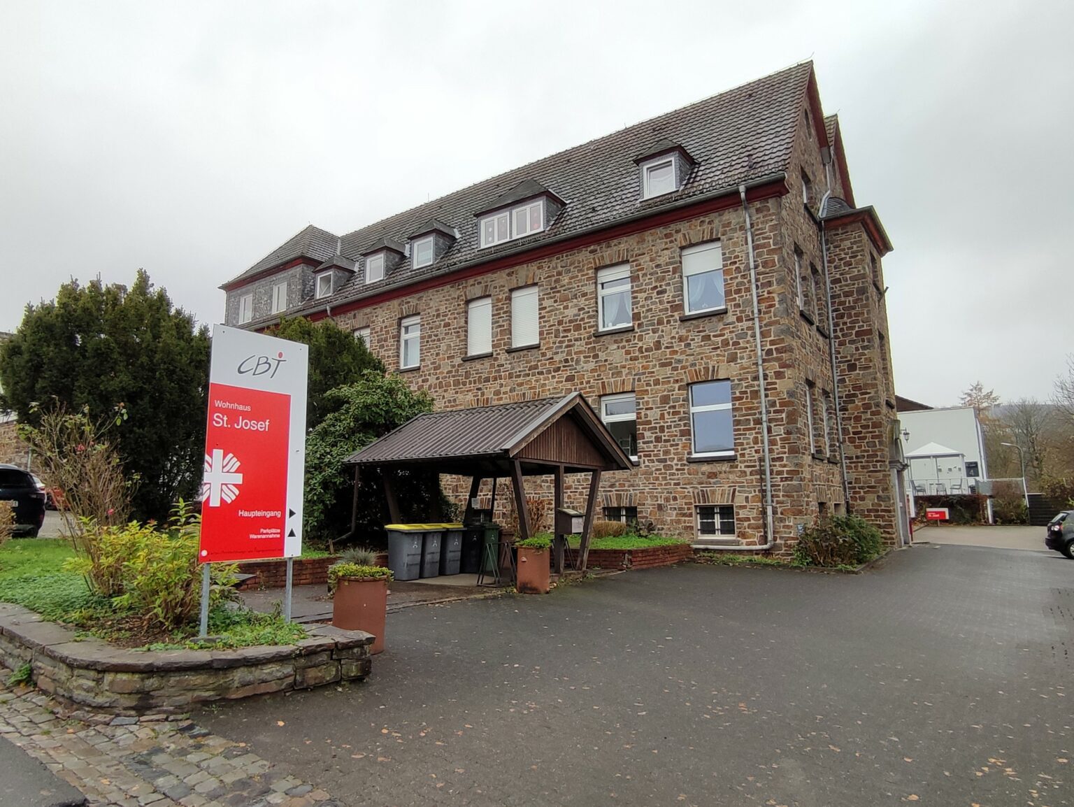 Mittelalterliches Steingebäude in Meckenheim mit Schild Wohnhaus St. Josef und Garten im Vordergrund.