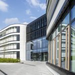 Moderne Bürogebäude mit Glasfassaden bei Sonnenschein, blauer Himmel im Hintergrund.