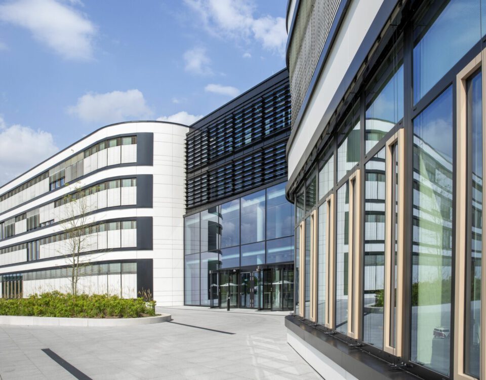 Moderne Bürogebäude mit Glasfassaden bei Sonnenschein, blauer Himmel im Hintergrund.