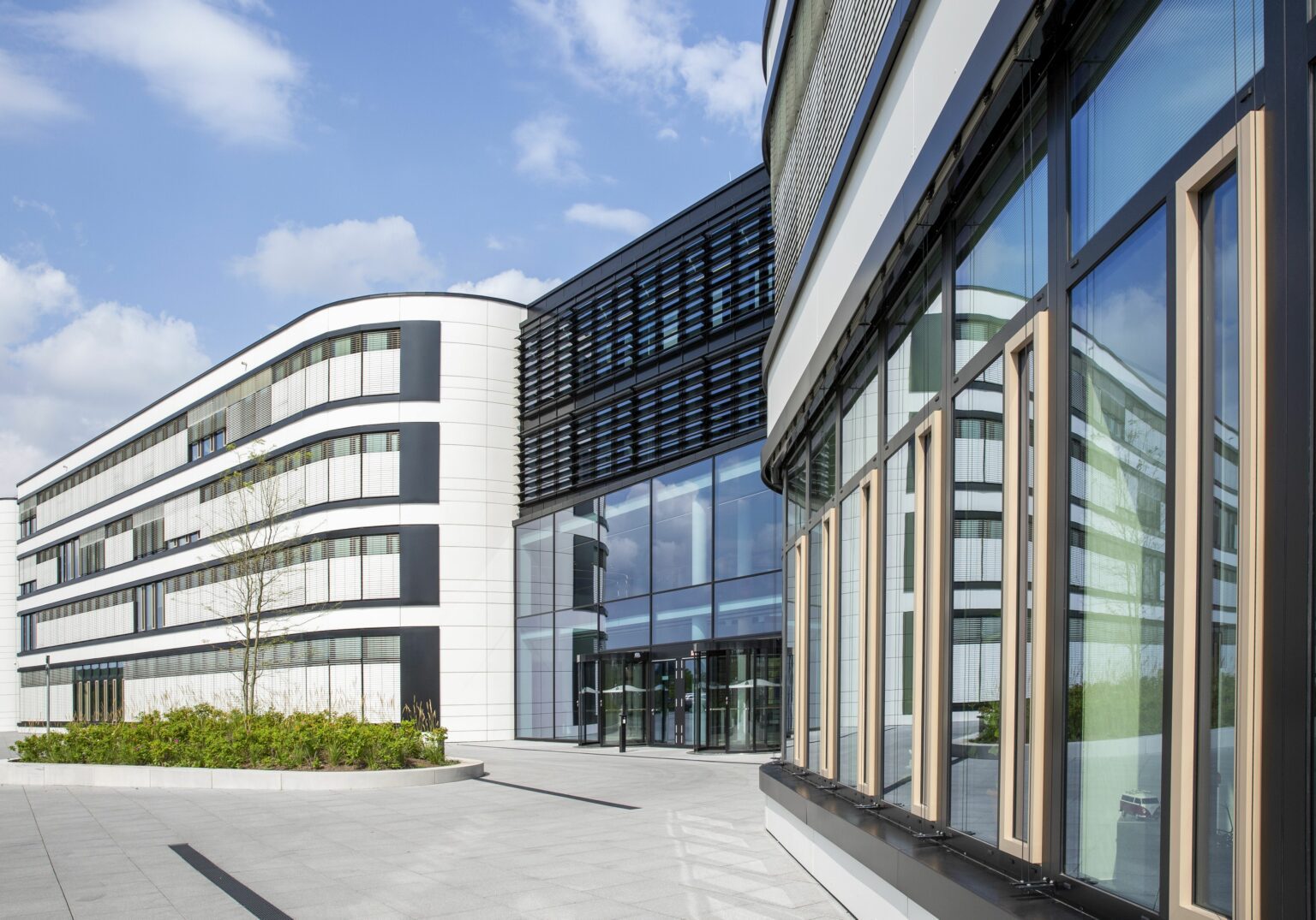 Moderne Bürogebäude mit Glasfassaden bei Sonnenschein, blauer Himmel im Hintergrund.