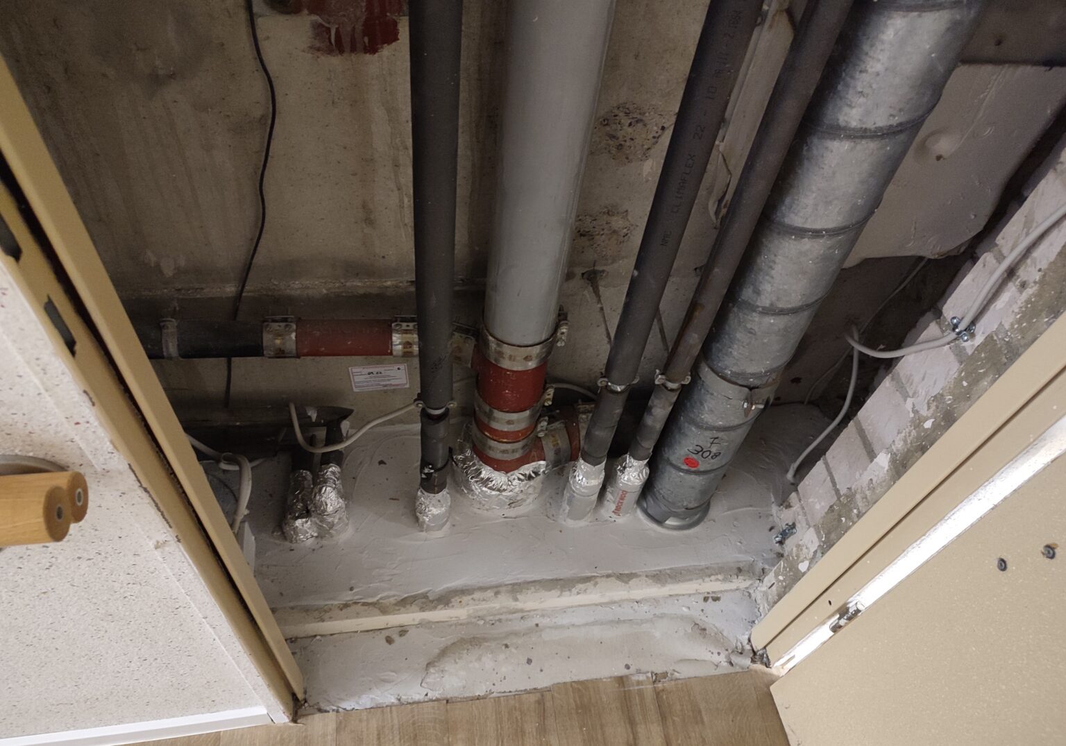 Rohrleitungssystem in einem Schacht mit verschiedenen Isolierungen und Verbindungsstücken für Gebäudeinstallation.