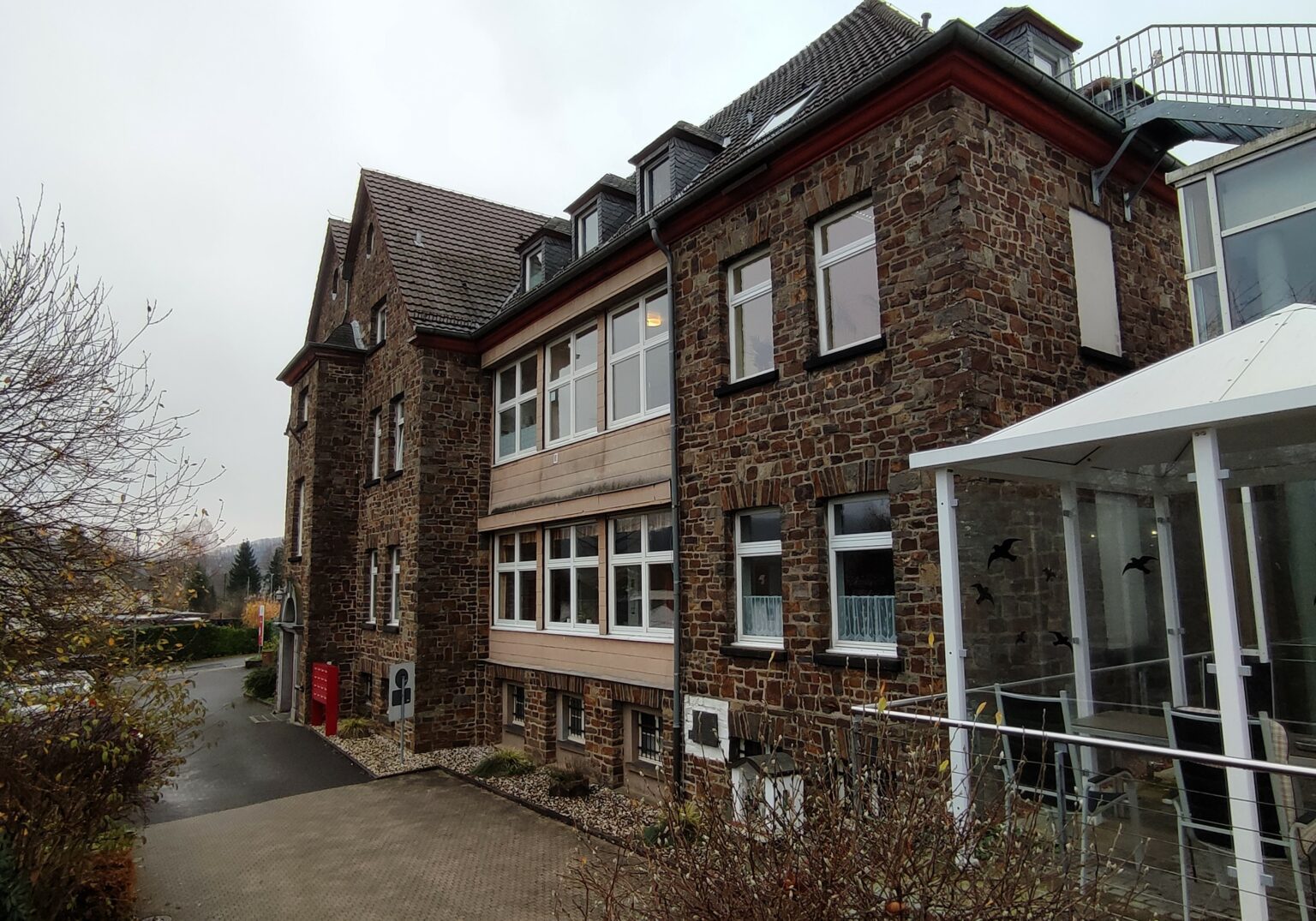 Historisches Backsteingebäude mit moderner Veranda und Dachfenstern an einem bewölkten Tag.