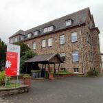 Altes Steingebäude des Wohnhauses St. Josef mit Schild und gepflegter Umgebung, bewölkter Himmel im Hintergrund.