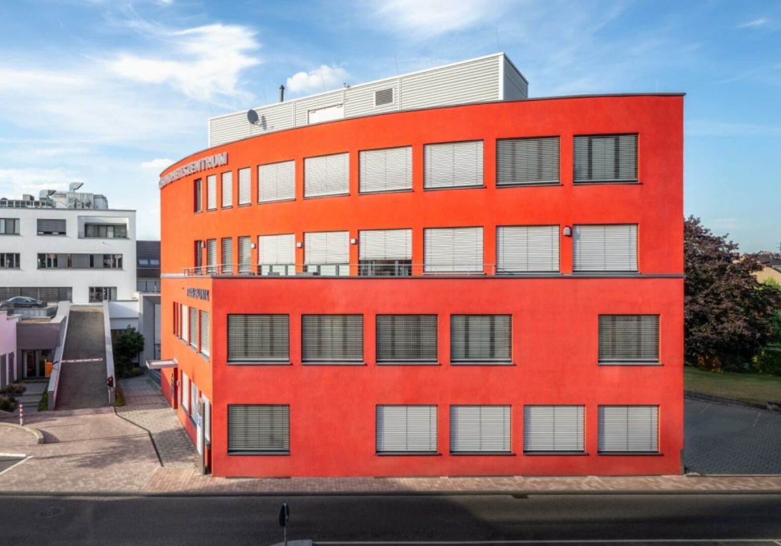 Modernes rotes Bürogebäude bei sonnigem Wetter, klarer blauer Himmel im Hintergrund.