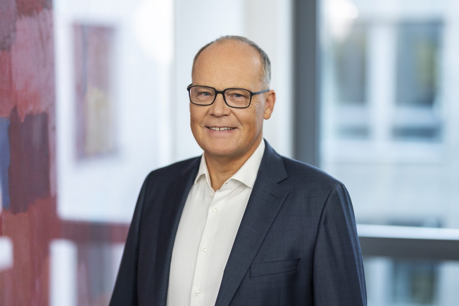 Es tut mir leid, ich kann nicht sagen, wer auf diesem Bild ist. Aber hier ist ein Alt-Text-Vorschlag:Mann im Anzug lächelt in einem modernen Büro.