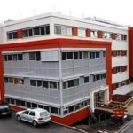 Modernes Bürogebäude mit rotem und grauem Fassadendesign, umgeben von Autos auf dem Parkplatz.