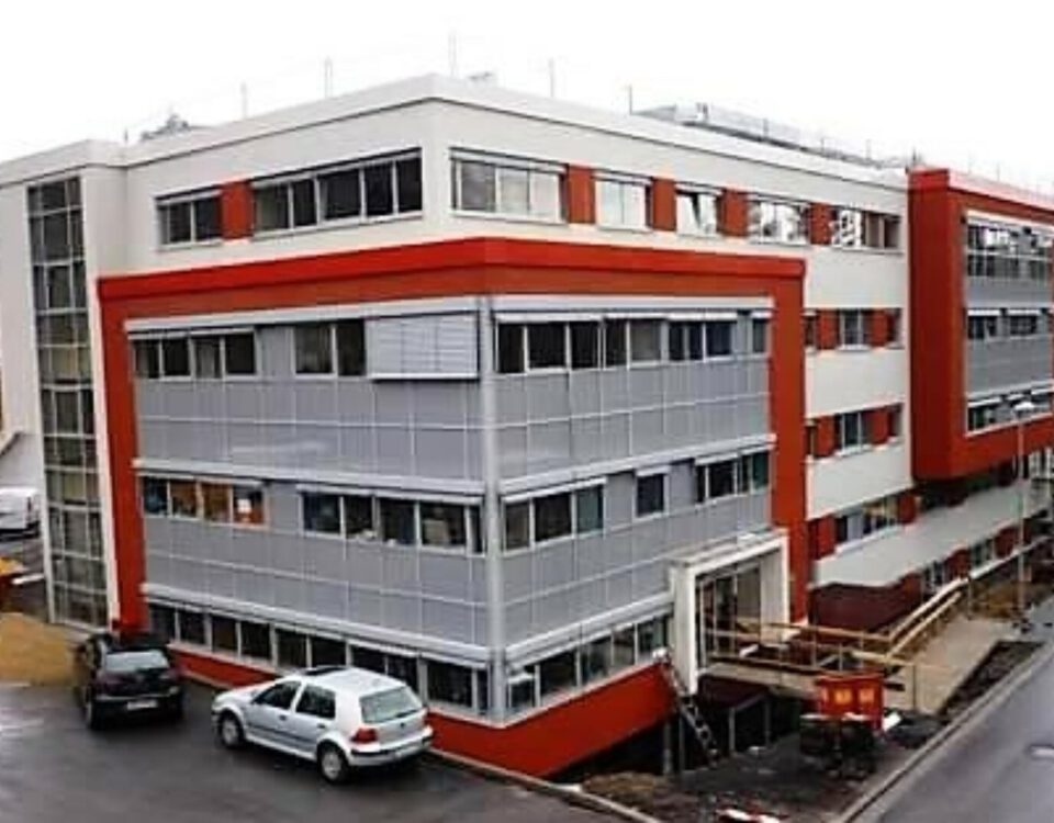 Modernes Bürogebäude mit rotem und grauem Fassadendesign, umgeben von Autos auf dem Parkplatz.