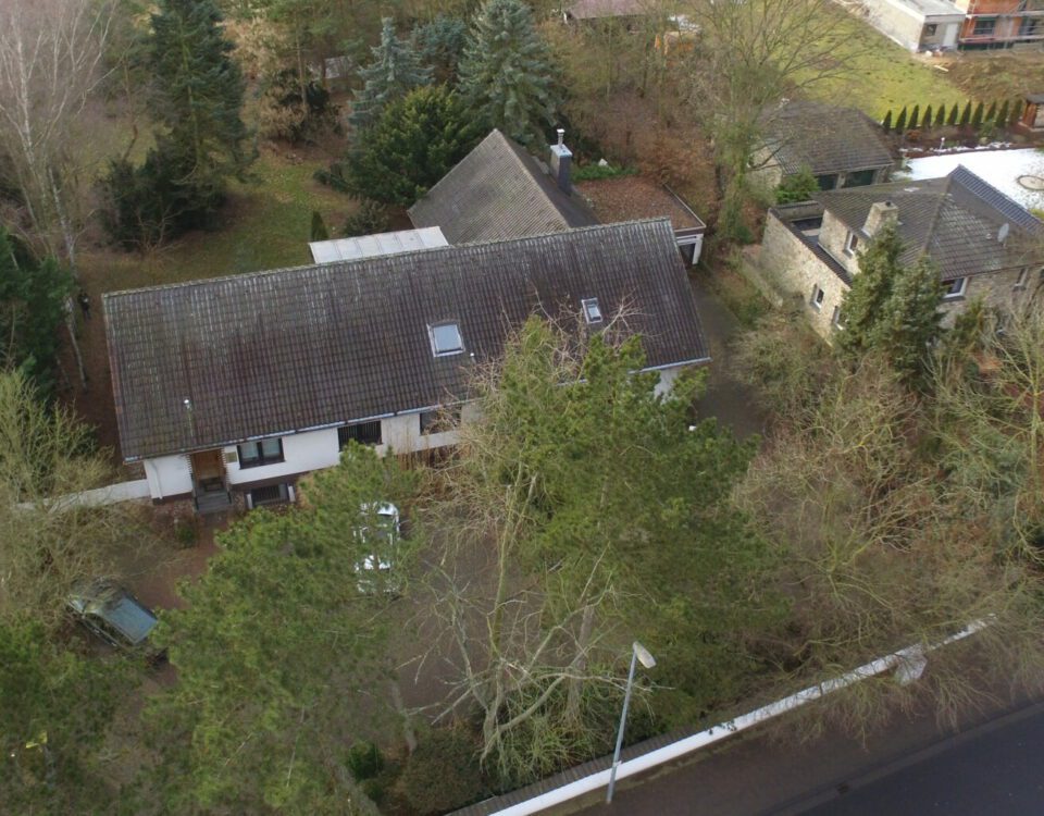 Luftaufnahme eines Einfamilienhauses mit einem großen Garten, umgeben von Bäumen, in einer ruhigen Nachbarschaft.