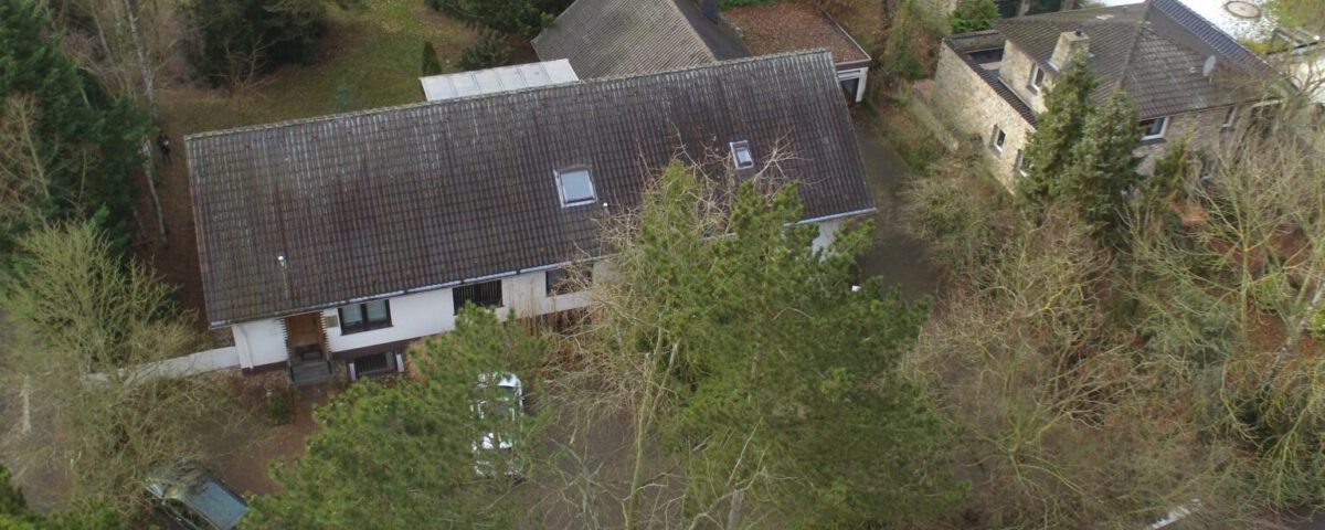 Luftaufnahme eines Hauses mit Garten, umgeben von Bäumen, in einem Wohngebiet.