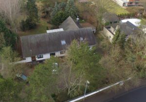 Luftaufnahme eines Hauses mit Garten, umgeben von Bäumen, in einem Wohngebiet.