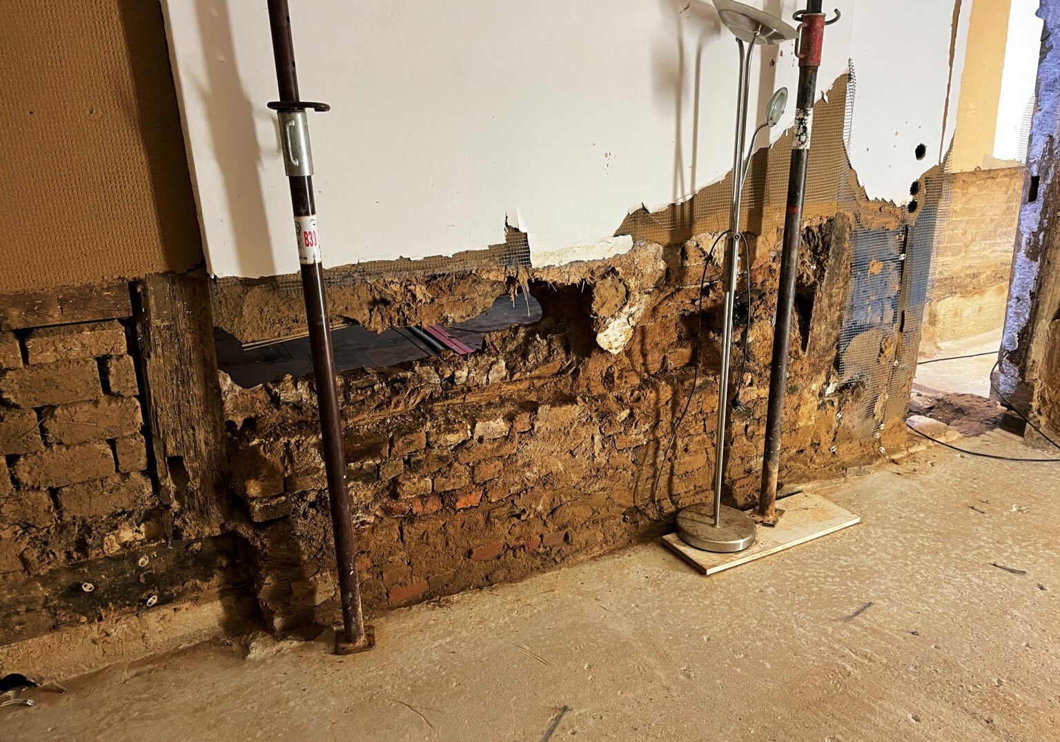 Beschädigte Altbauwand mit freiliegenden Ziegeln, gestützt durch Metallstangen.