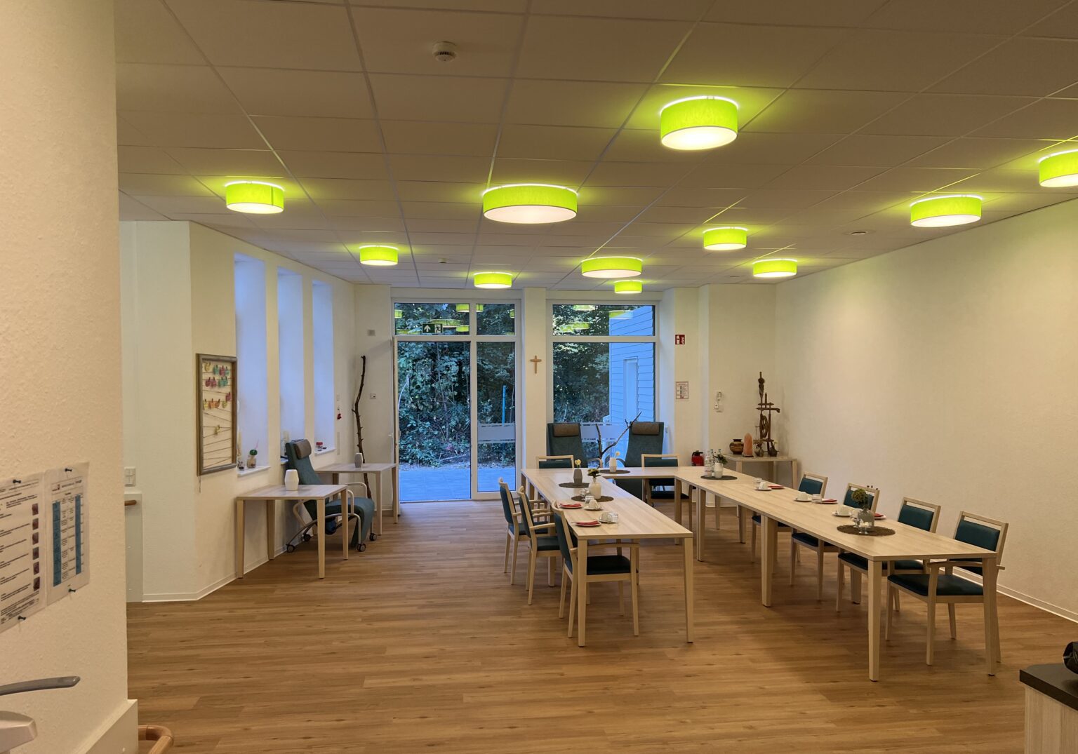Heller Besprechungsraum mit Holztischen, grüner Beleuchtung und großen Fenstern mit Blick ins Freie.