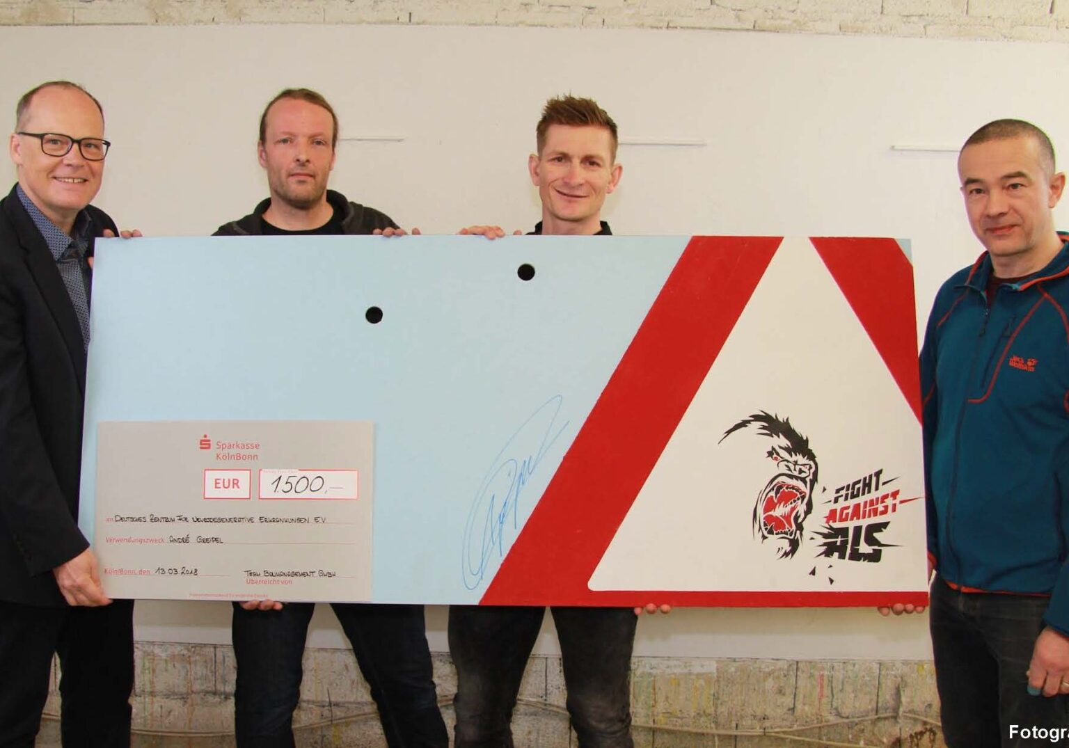 Vier Männer überreichen einen symbolischen Scheck über 1500 Euro für den Kampf gegen ALS.