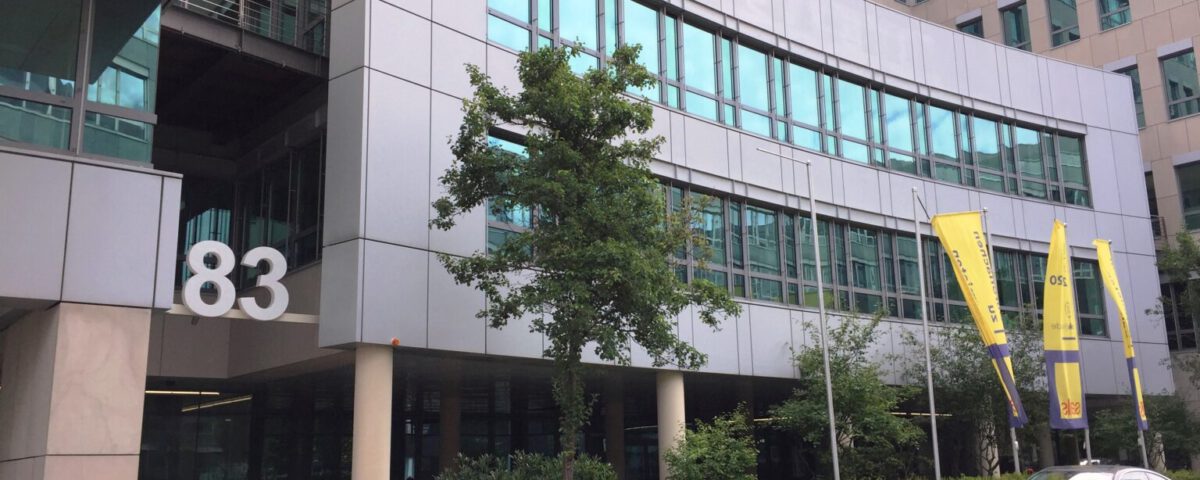 Bürogebäude mit der Nummer 83, moderne Architektur, gelbe Fahnen und parkendes Auto im Vordergrund.