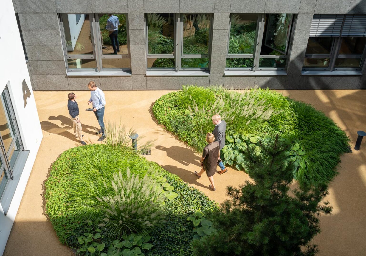 Innenhof mit grünen Pflanzen und Menschen, die sich unterhalten und spazieren gehen. Moderne Büro-Architektur.