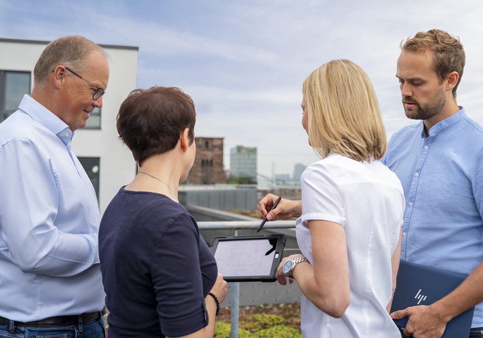 Gruppe von Kollegen diskutiert Baupläne mit Tablet im Freien auf einer Dachterrasse.