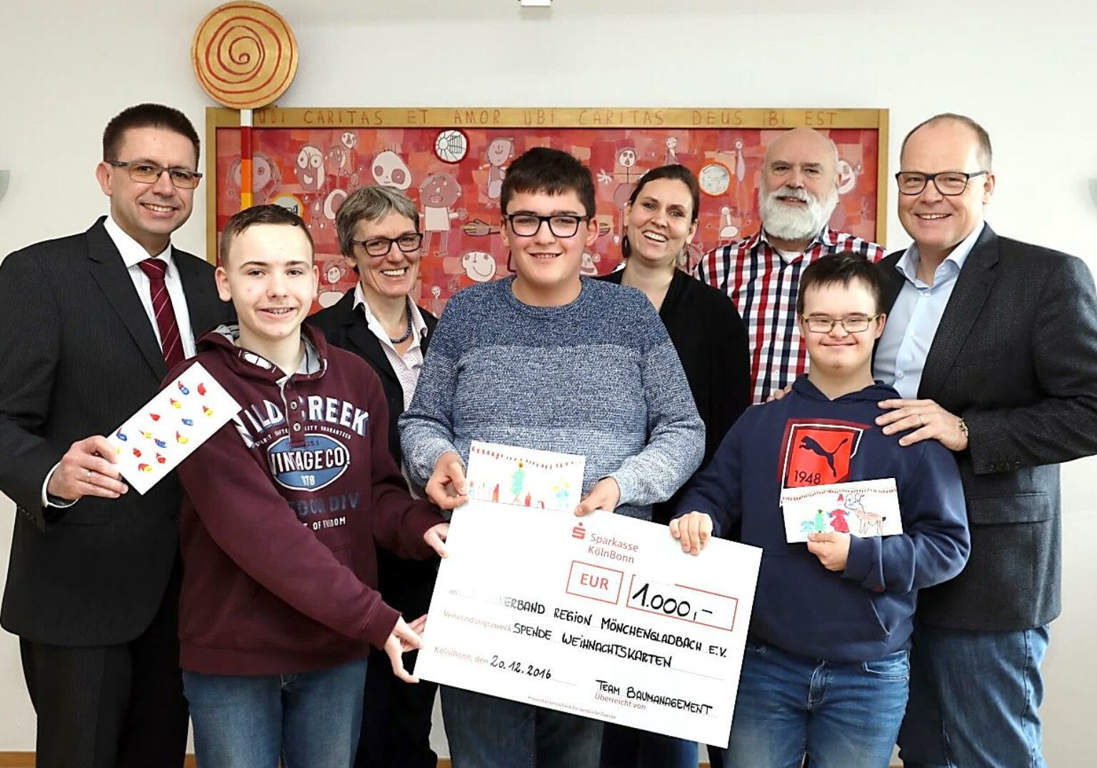 Gruppe von Menschen hält einen Spendenscheck in Höhe von 1000 Euro in einer feierlichen Übergabe.