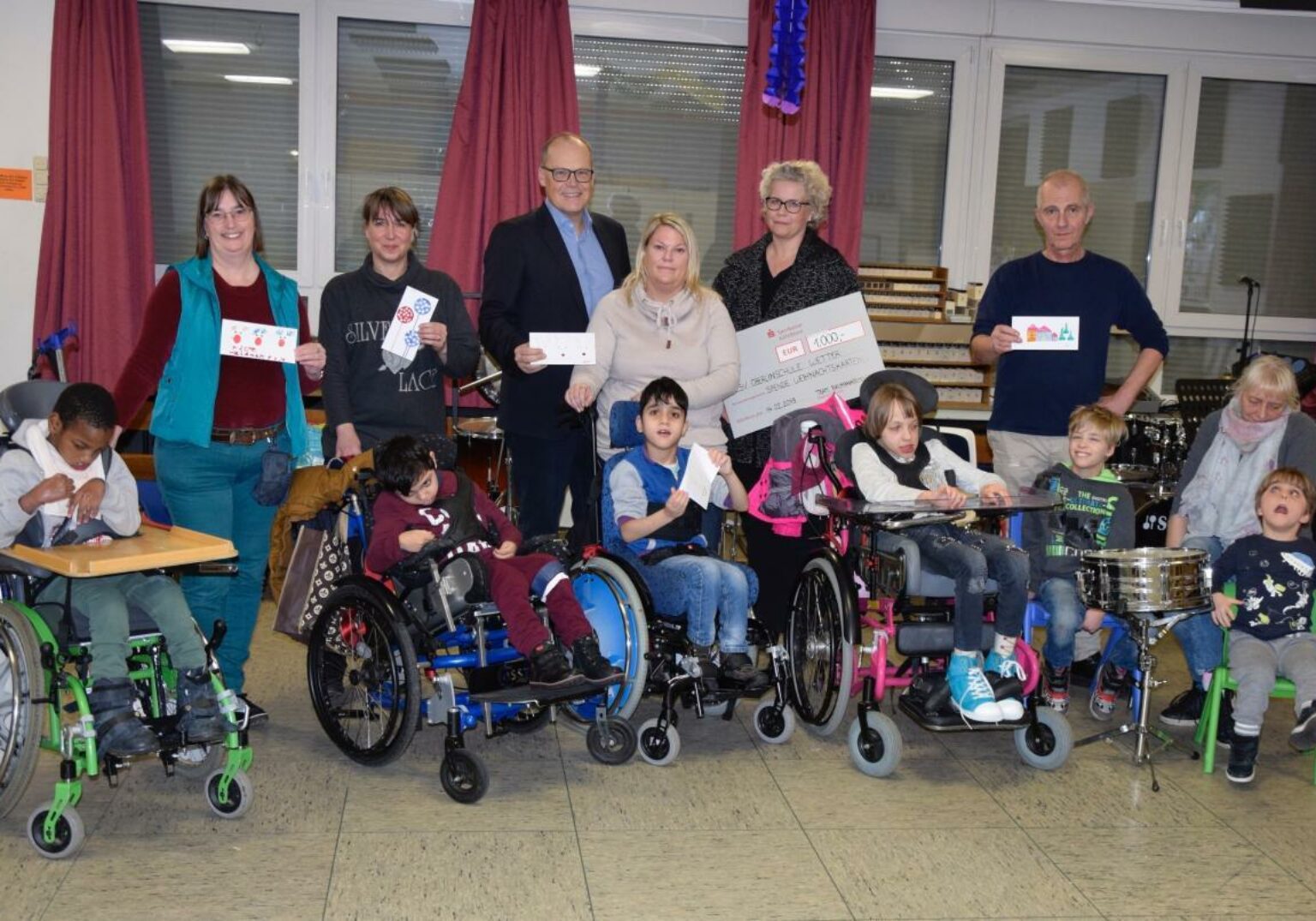Gruppe von Kindern und Erwachsenen bei einer Spendenübergabe, einige in Rollstühlen, fröhliche Atmosphäre.