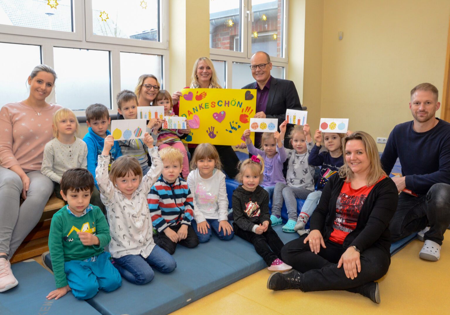 Gruppe von Kindern und Erwachsenen in einem Klassenzimmer mit einem Dankeschön-Plakat und gebastelten Karten.