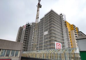 Hochhaus mit Baugerüst und Kran im Umbau, moderne Architektur, bewölkter Himmel im Hintergrund.