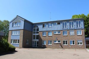 Moderner Bürogebäudekomplex aus Backstein mit blauen Paneelen an sonnigem Tag, umgeben von Natur.