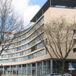 Moderne Architektur eines geschwungenen Bürogebäudes mit Glasfassade an einem sonnigen Tag.