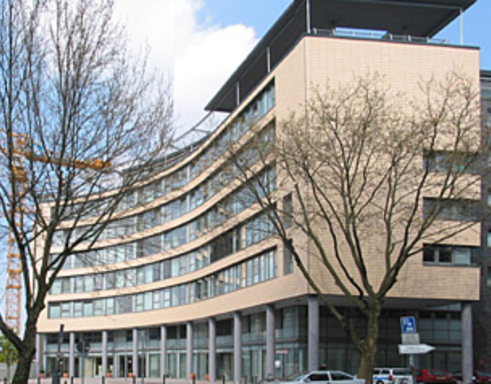 Moderne Architektur eines geschwungenen Bürogebäudes mit Glasfassade an einem sonnigen Tag.